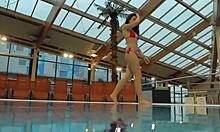 Katy Sorokas nada desnuda junto a la piscina en fondos rojos de bikini